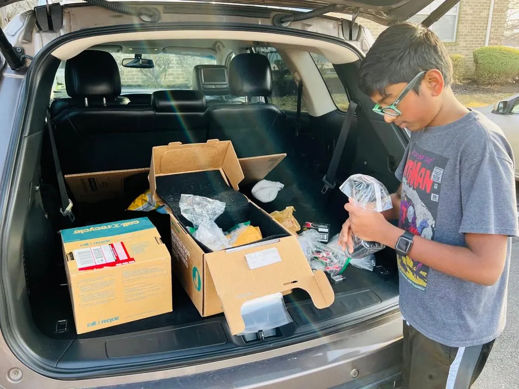 Nihal sorting batteries in front of a car with its trunk open: he is getting the batteries ready for shipment. 
