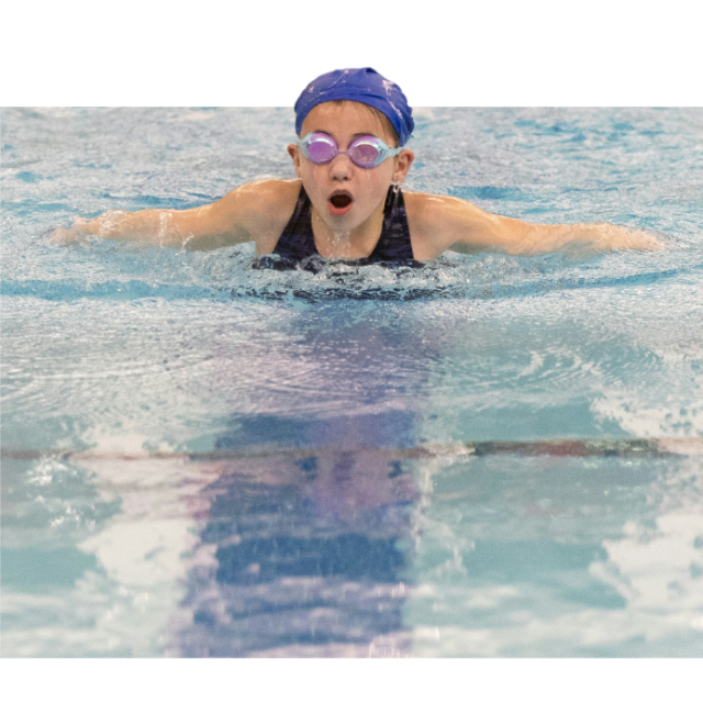 A child wearing a purple swim cap and swim goggles comes up for a breath while swimming.