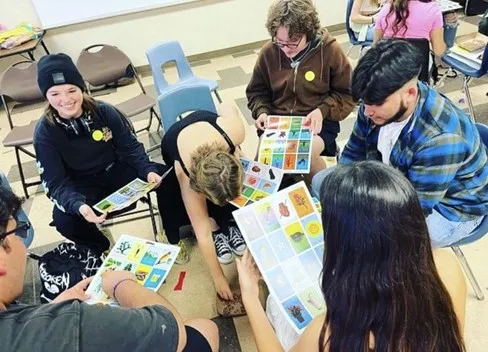 Group of students playing Loteria at a MiSendero cultural exchange event. Students are sitting on chairs in a small circle holding colorful papers.