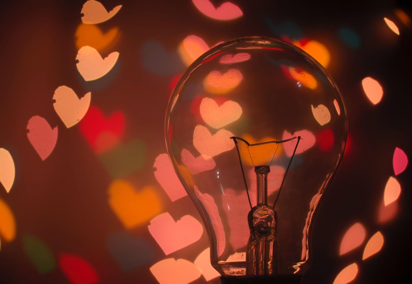Close-up of a lightbulb on the right side of the image, with pink and red blurry heart lights in the background