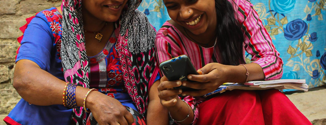 Two girls sit on steps and laugh while on a mobile phone.