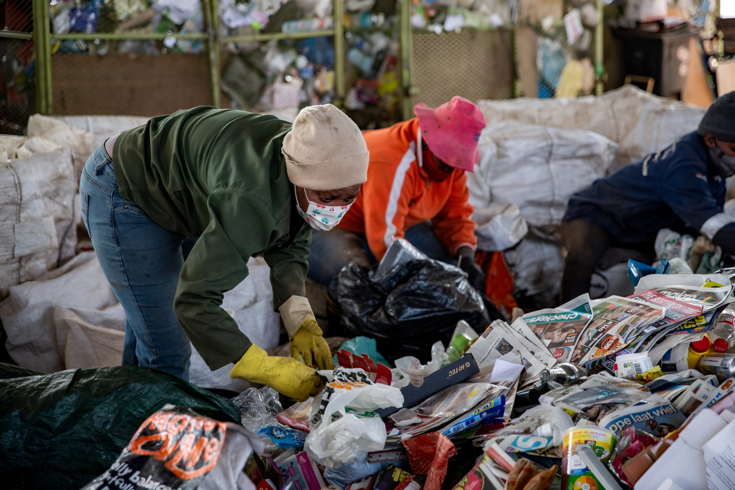 Two women wearing face masks pick through large piles of trash