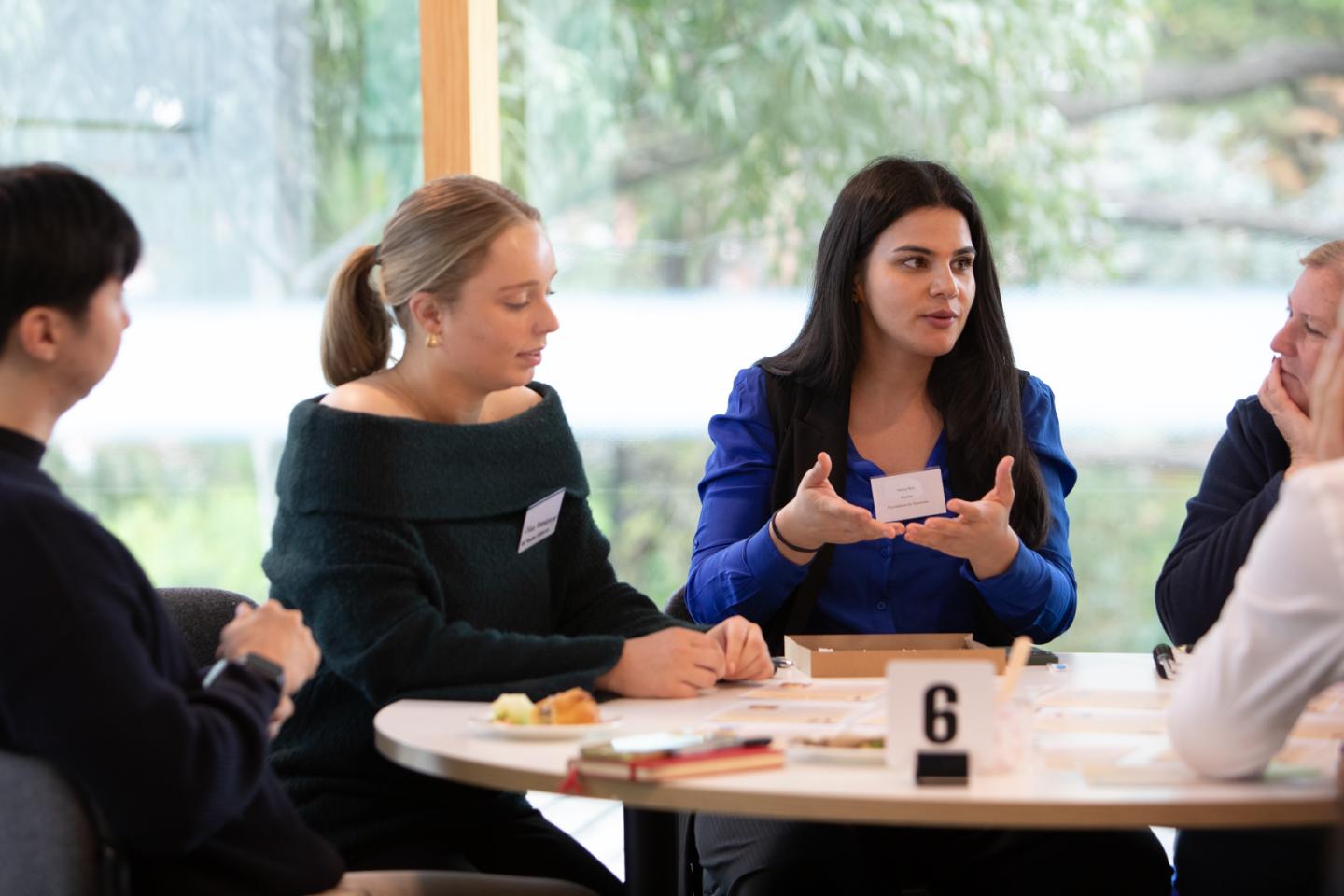 A small group speaks at a table. A woman in a blue blazer has the groups attention.