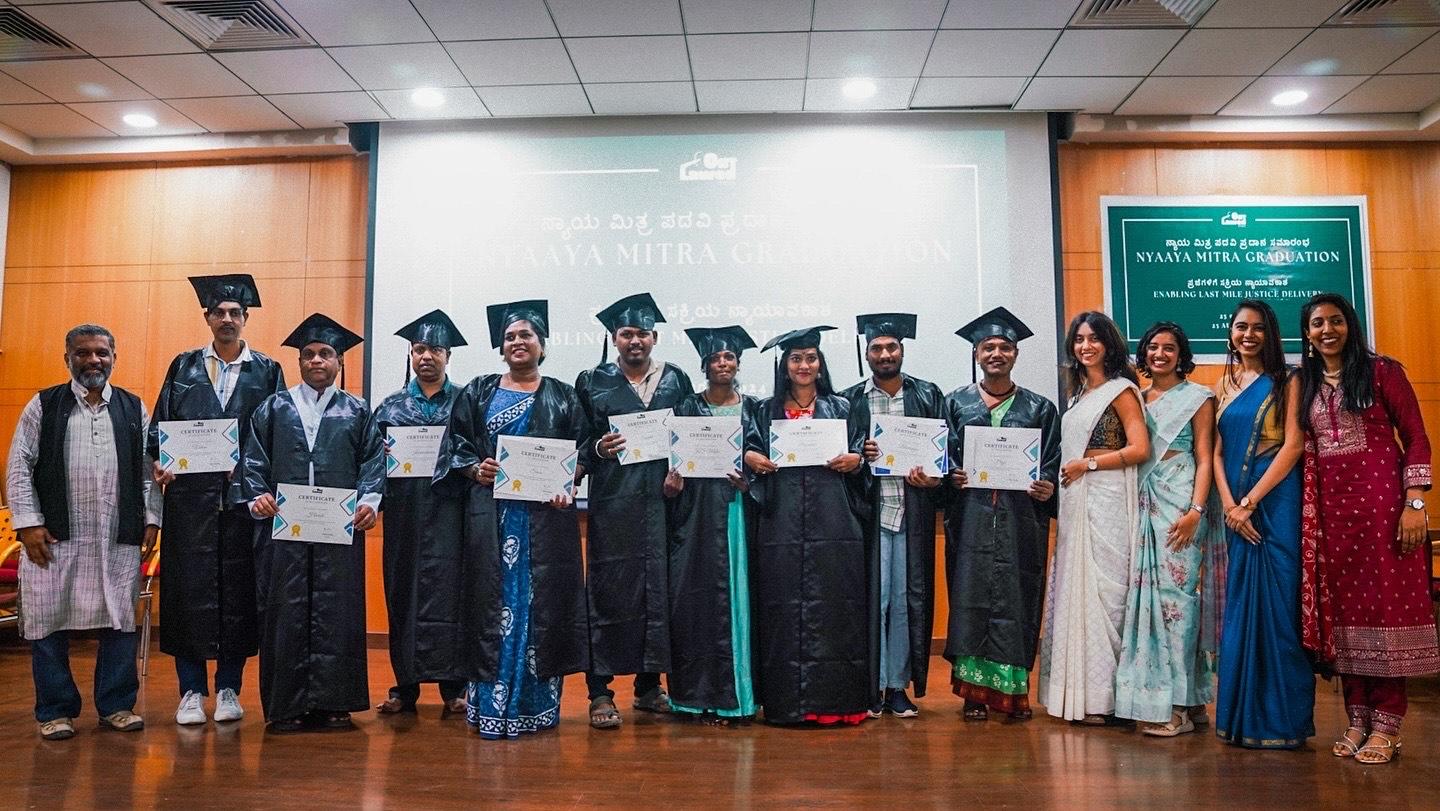 Students stand in a line holding up diplomas or certificates. They are all wearing graduation gowns and caps.