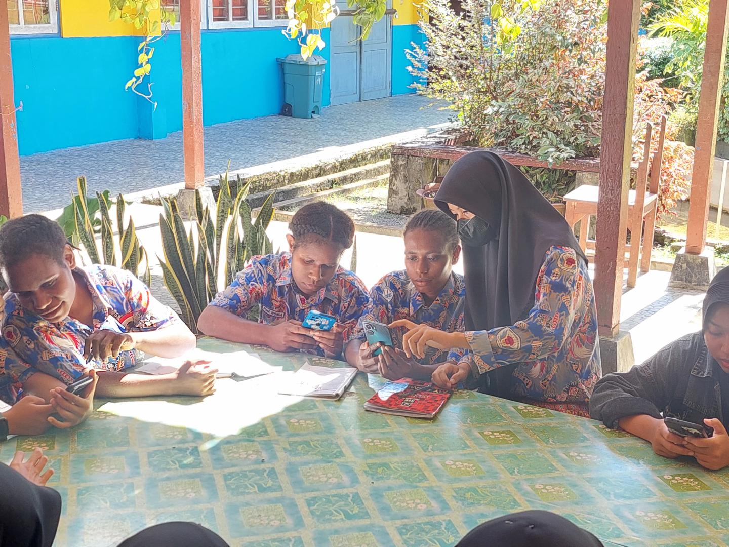 A woman wearing a hijab helps a students at a table with school work.