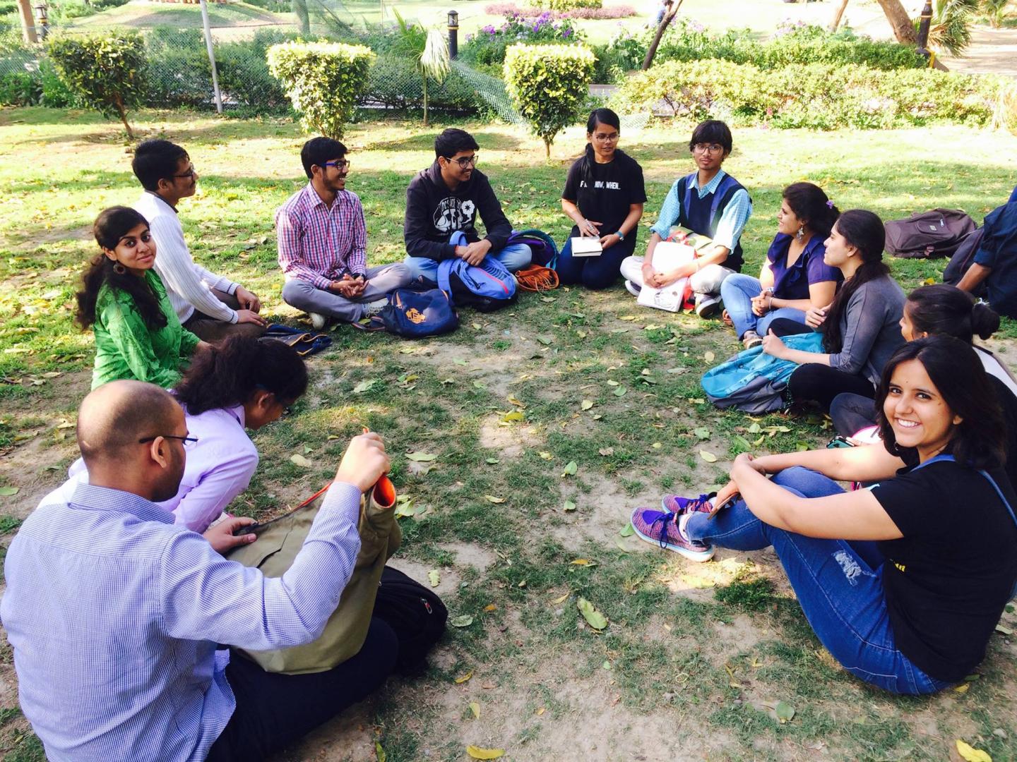 A group of students sit in a circle in a grassy field.